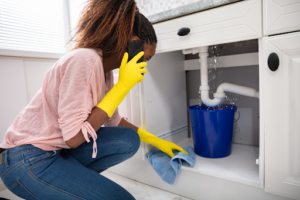 A woman cleaning up a plumbing leak and calling for emergency plumbing services in Houston, TX.