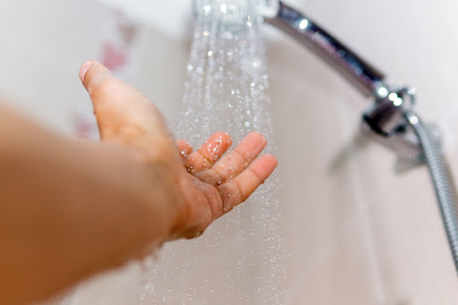 A person putting their hand under a running showerhead.