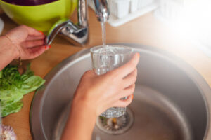A person using a kitchen faucet to fill a glass of water.