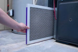 A person touching an air filter next to a furnace.